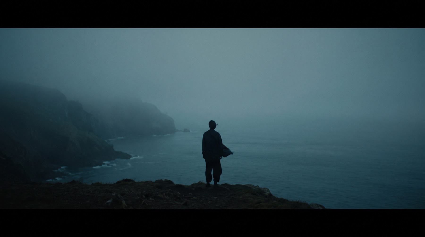 A person stands easy on a coastal headland at sunset, under an immense calm sky.