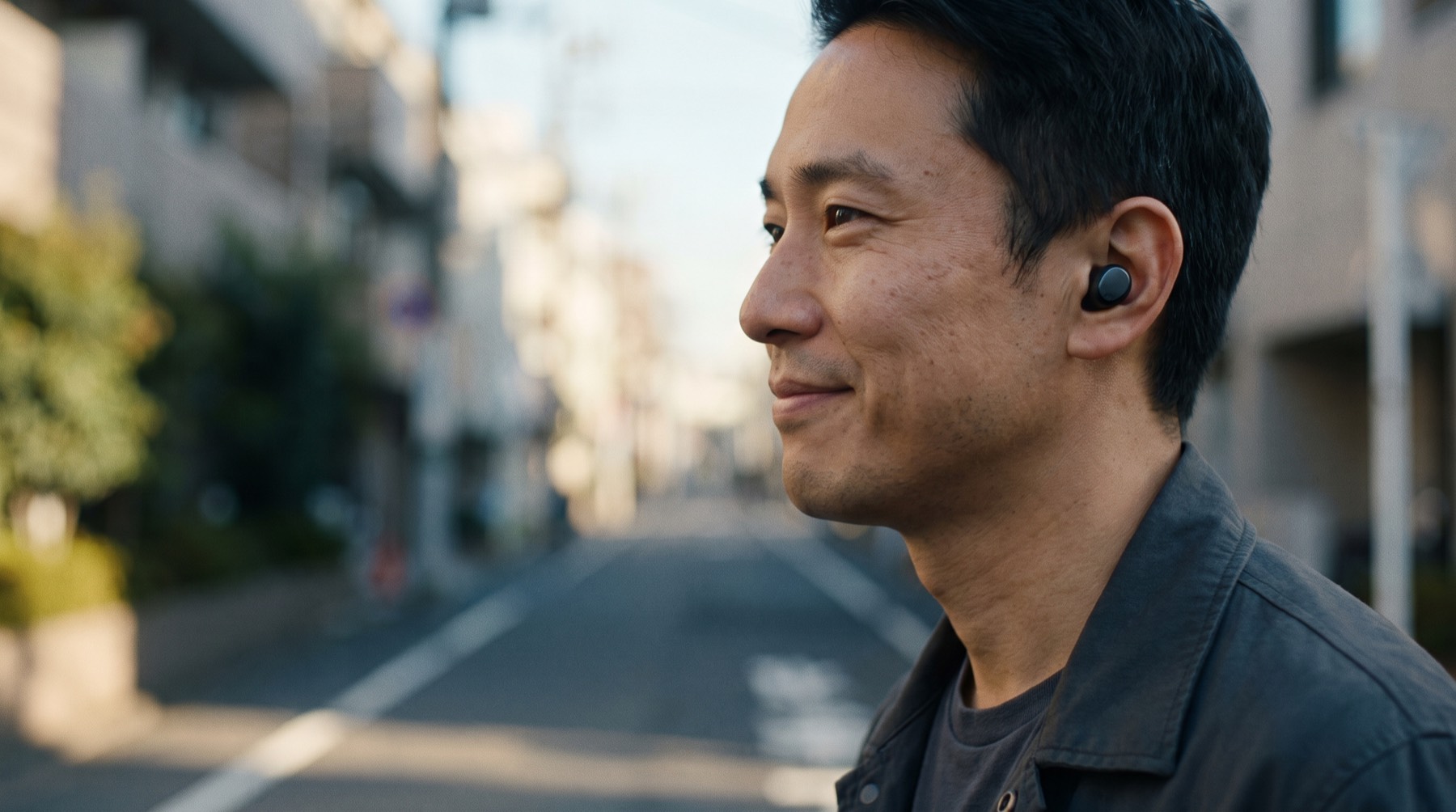 A relaxed man mid-sentence at golden hour, one earbud in, city lights softly blurred behind.